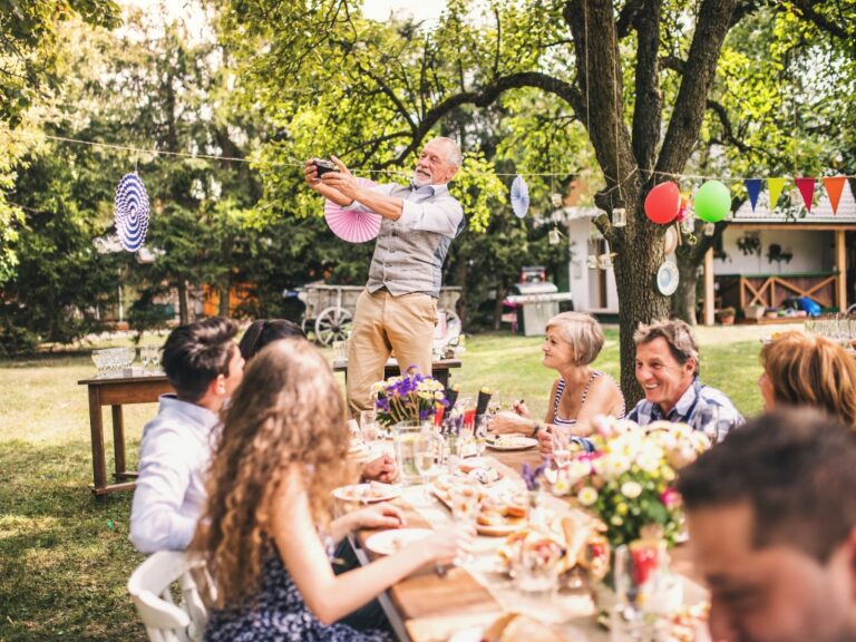 Mehrere Generationen feiern gemeinsam im Garten an einem langen Tisch – Symbolbild für Familienfeste im Frühling mit Rücksicht auf besondere Ernährungsbedürfnisse.