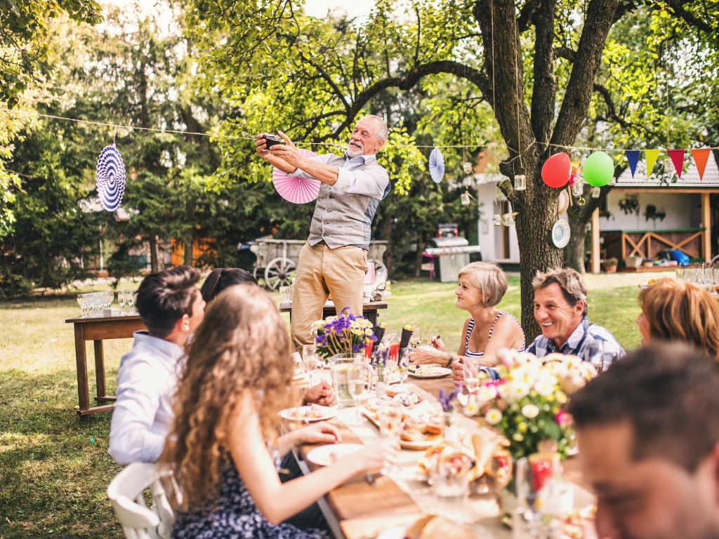 Mehrere Generationen feiern gemeinsam im Garten an einem langen Tisch – Symbolbild für Familienfeste im Frühling mit Rücksicht auf besondere Ernährungsbedürfnisse.