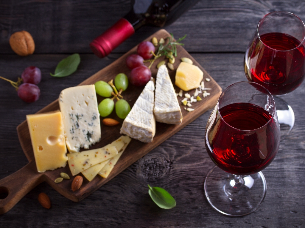 Käseplatte mit verschiedenen Sorten und zwei Gläsern Rotwein – typische histaminreiche Lebensmittel bei Histaminunverträglichkeit.