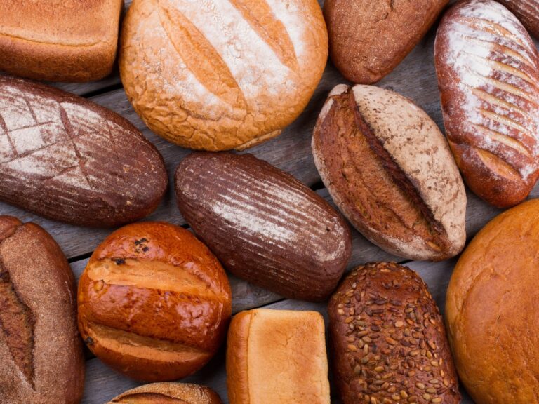 Verschiedene Sorten glutenhaltiger Brote und Brötchen auf Holzuntergrund – Symbolbild für glutenhaltige Lebensmittel bei Glutensensitivität.