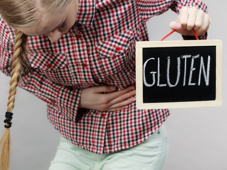 Frau mit Bauchschmerzen durch Glutenunverträglichkeit hält Tafel mit dem Wort Gluten
