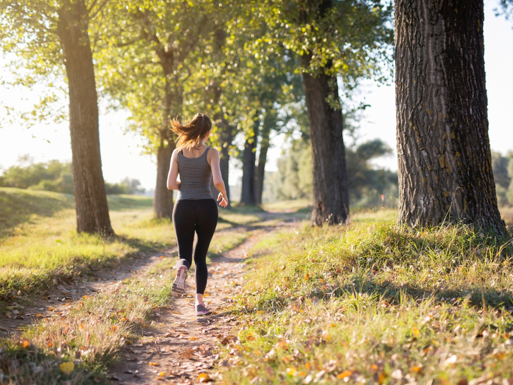 Frau macht Sport und hat keine Beschwerden mit ihren Nahrungsmittelunverträglichkeiten. Sie läuft auf einem kleine Feldweg lang.