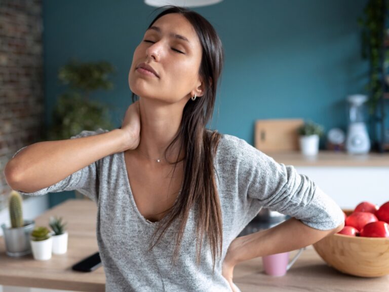 Frau hält sich ihren Hals, da sie aufgrund von Stress und einer Histaminintoleranz Nackenschmerzen hat. Sie verzieht schmerzerfüllt ihr Gesicht.