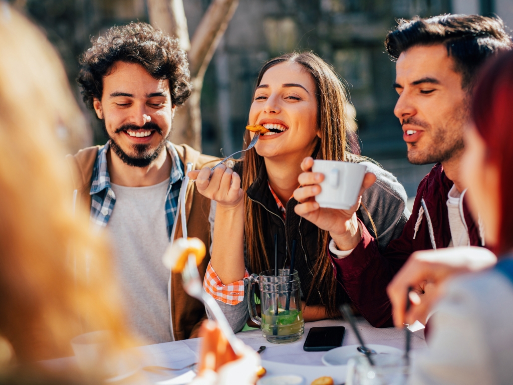 Freunden treffen sich im Restaurant. Eine Person hat eine Nahrungsmittelunverträglichkeit, was sie aber nicht abhält dort essen zu gehen. Auf dem Bild sind alle glücklich und lächeln.