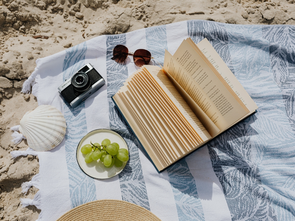 Auf dem Bild sieht man eine Muschel, eine Kamera, eine Brille und ein Buch zu liegen. Symbolisch soll dies für Entspannung und Leichtigkeit im Sommer, auch für Menschen mit Nahrungsmittelunverträglichkeiten sprechen.