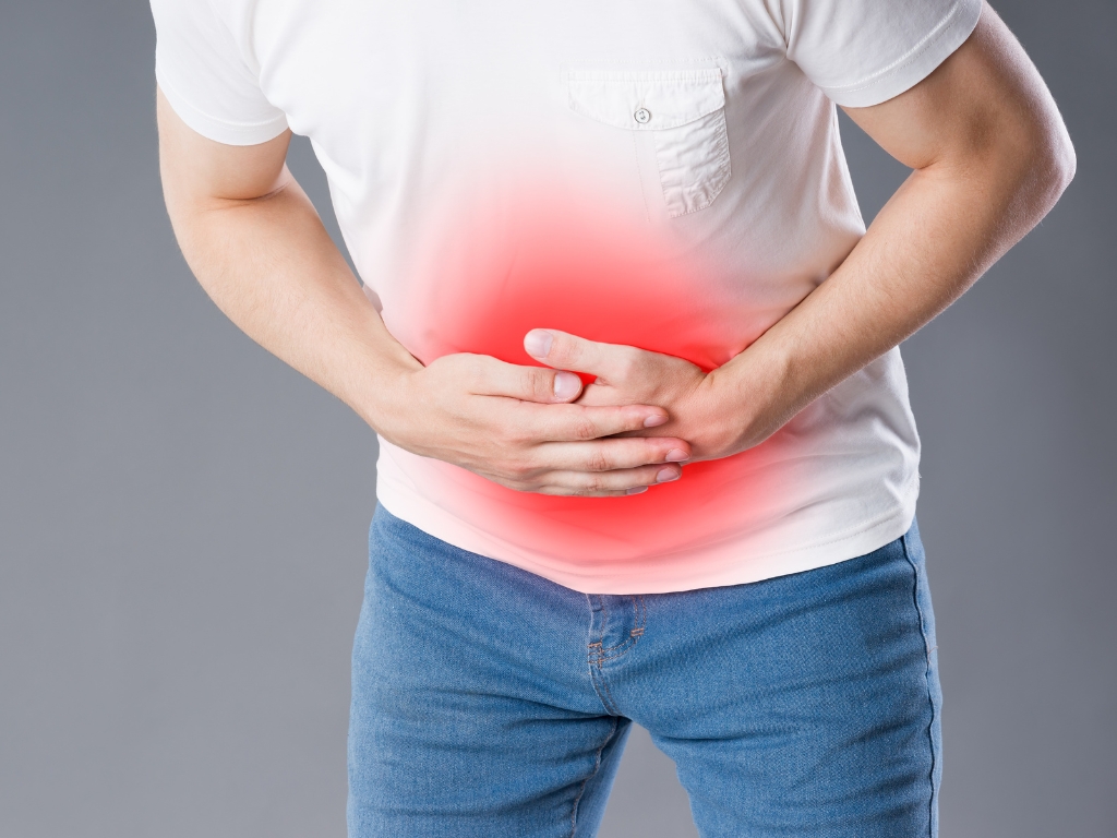 Mann hält sich seinen Bauch, weil er wegen Stress und Nahrungsmittelunverträglichkeiten Bauchschmerzen hat.