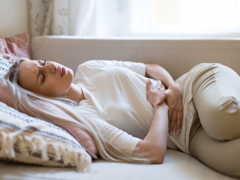 Frau mit Bauchschmerzen hält sich den Unterbauch – Symbolbild für Nahrungsmittelunverträglichkeit