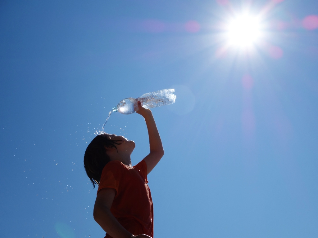 Junge kühlt sich mit Wasser in der prallen Sonne ab. Ein Sinnbild dafür, dass auch Menschen mit Intoleranzen die Hitze gut überstehen.