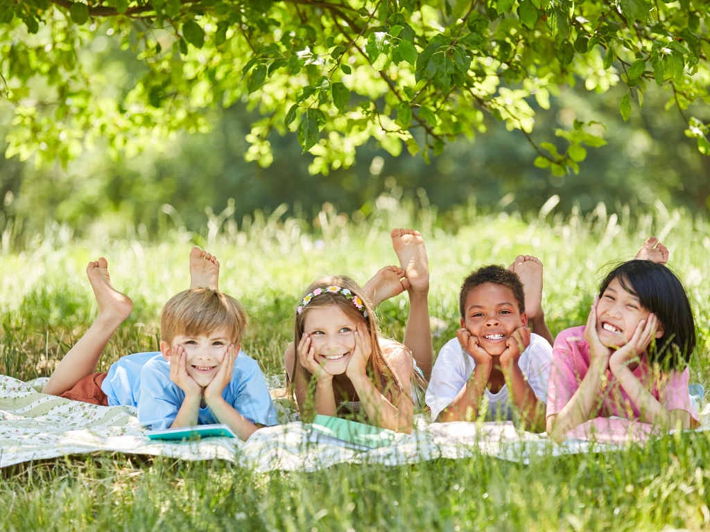 Kinder mit Intoleranzen liegen entspannt auf einer Decke. Ein Baum liefert ihnen Schatten und sie sehen glücklich aus.