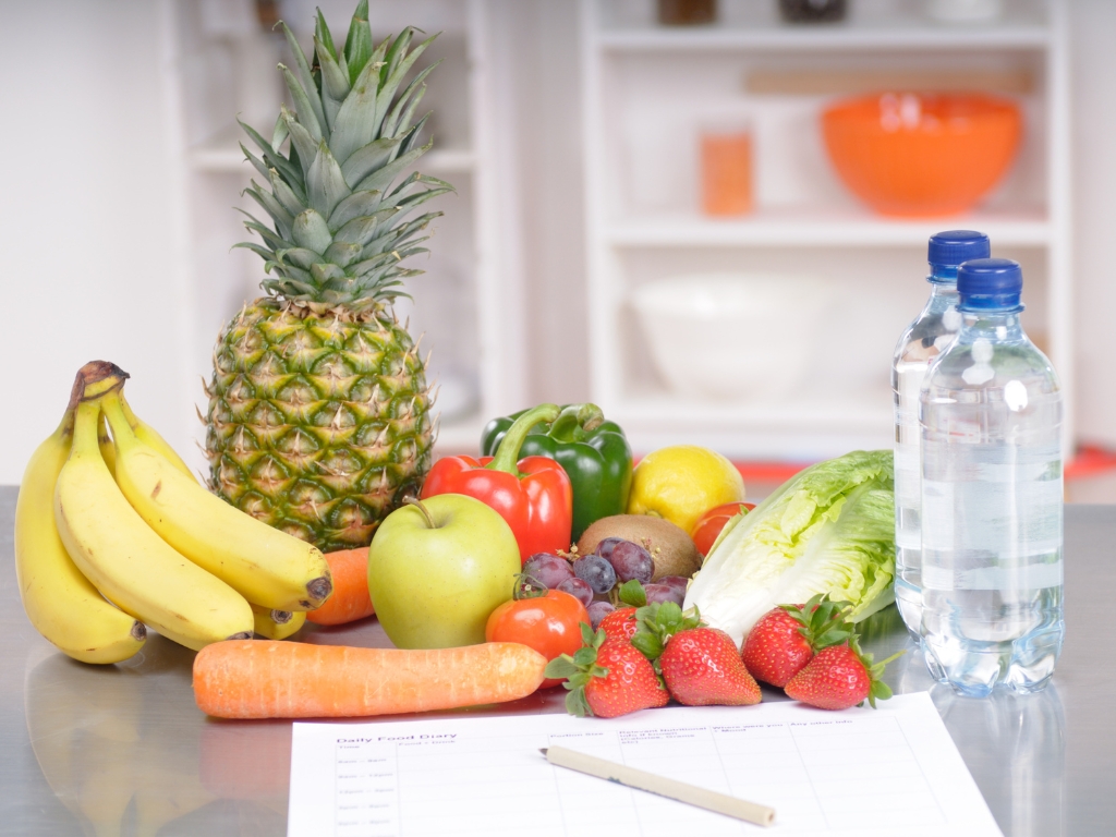 Im Bild sind ein paar Obst und Gemüsesorten zu erkennen und davor liegt ein Ernährungstagebuch. Dies soll Menschen mit Unverträglichkeiten helfen, ihre Symptomatik besser zu verstehen.
