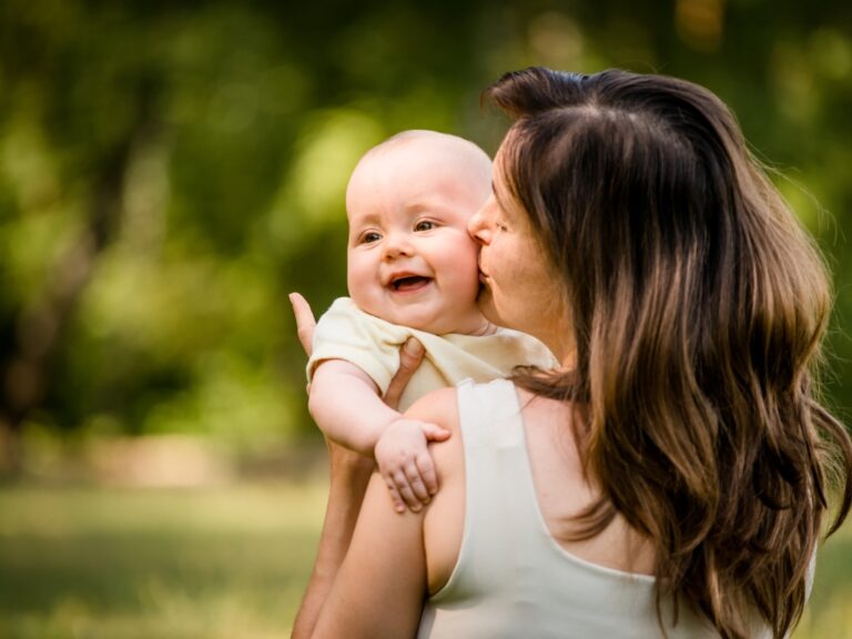 Abgebildet ist eine Mutter mit Intoleranzen, welches ihr Baby auf dem Arm hält und liebevoll küsst. Trotz ihrer Unverträglichkeiten kann sie ihr Kind ganz normal stillen.
