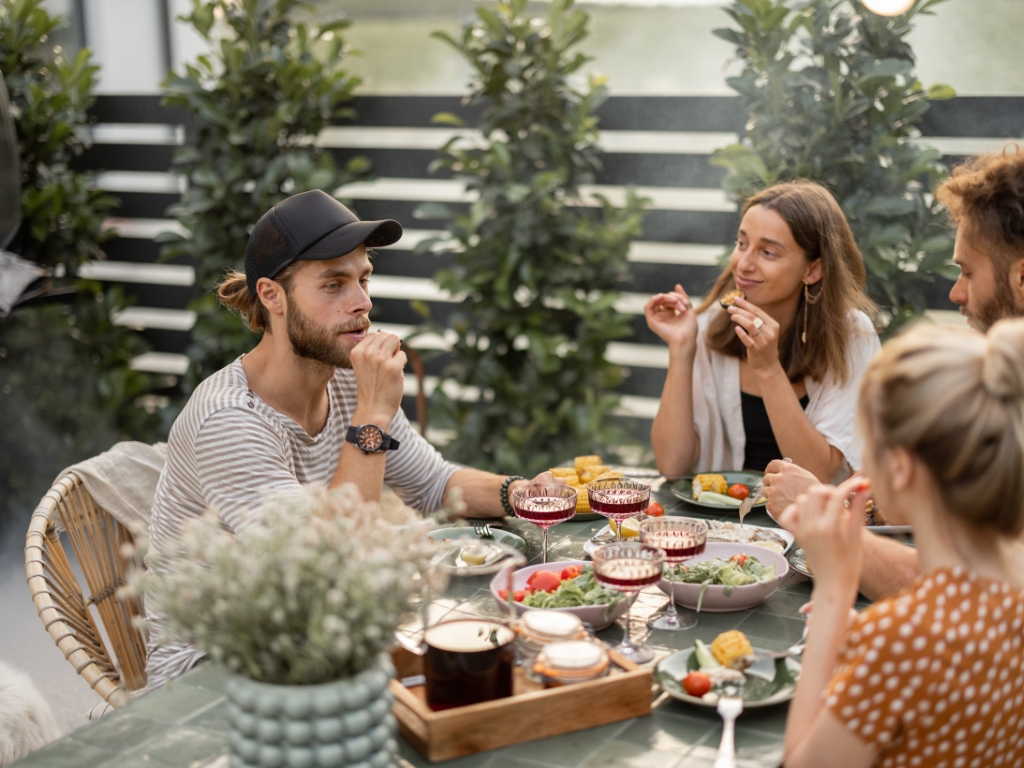 Ein entspannter Abend im Freundeskreis: Vier Menschen genießen gemeinsam ein verträgliches Essen im Freien. Das Bild zeigt, wie geselliges Essen auch bei Unverträglichkeiten möglich ist – mit guter Vorbereitung, gegenseitiger Rücksichtnahme und leckeren, gut verträglichen Speisen.