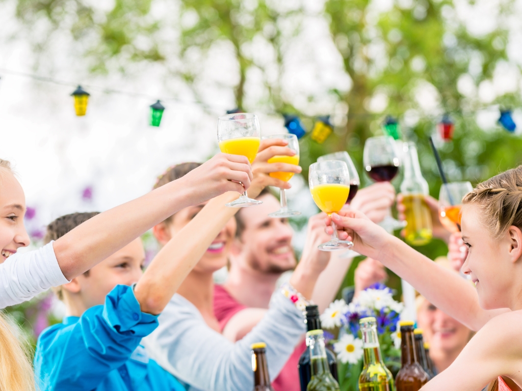 Eine fröhliche Gruppe junger Menschen stößt bei einer spätsommerlichen Gartenparty mit verträglichen Getränken an – zum Beispiel alkoholfreien Cocktails, histaminarmen Säften und Wasser. Die Stimmung ist entspannt und inklusiv, auch für Gäste mit Nahrungsmittelunverträglichkeiten.