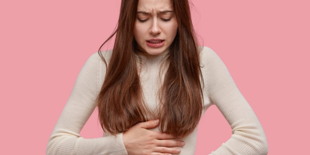 7 Junge Frau mit schmerzverzerrtem Gesicht hält sich den Bauch – Symbolbild für Magen-Darm-Beschwerden bei Histaminintoleranz.